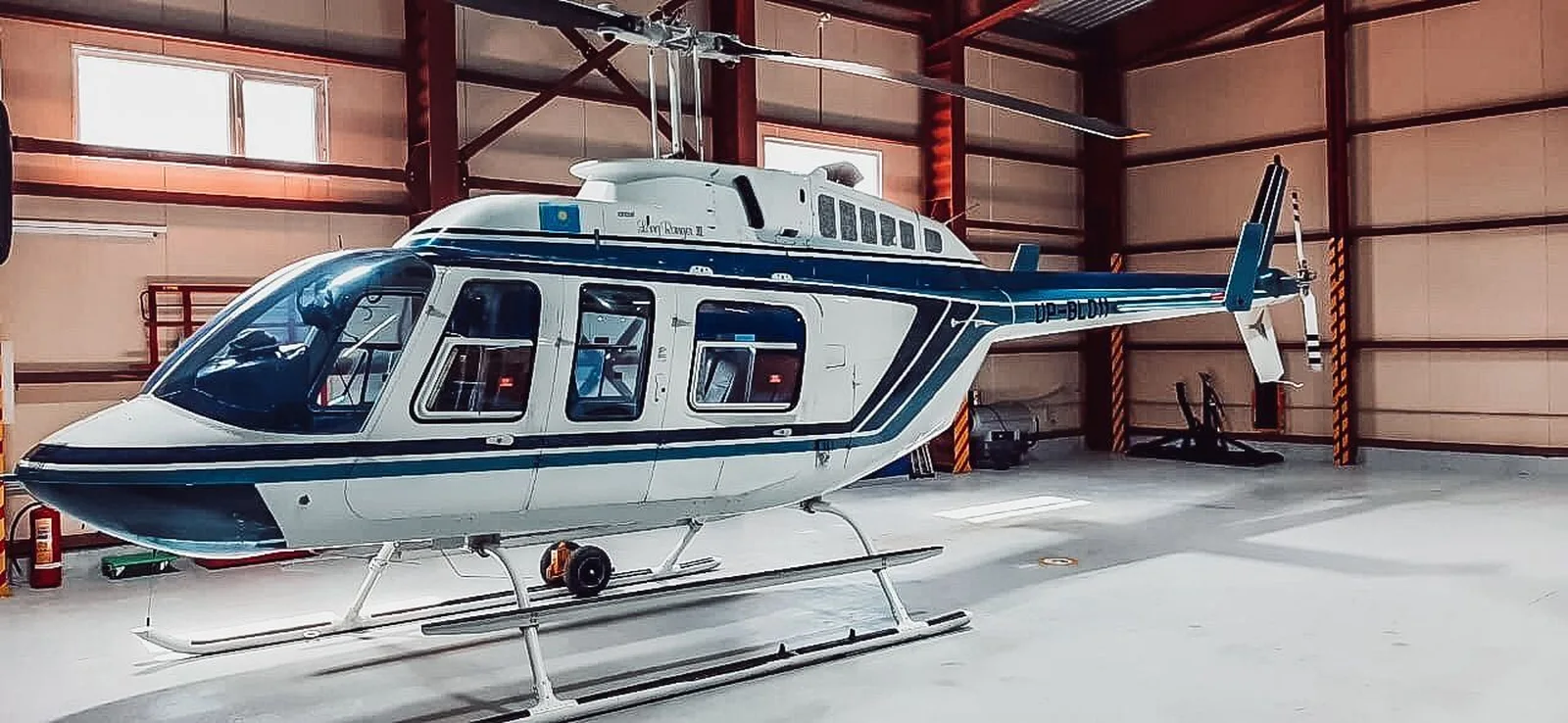 White and blue Bell Long Ranger helicopter parked inside a hangar